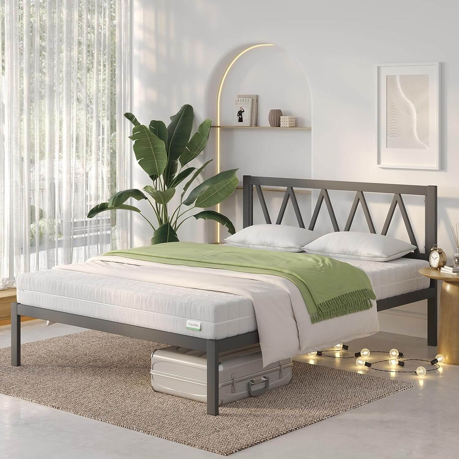 Dark gray metal bed frame with geometric headboard, white bedding, green throw blanket. Modern bedroom style.